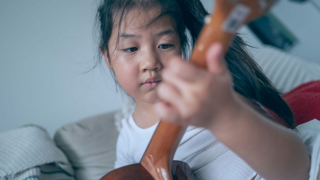 Young girl plays the ukulele intently.