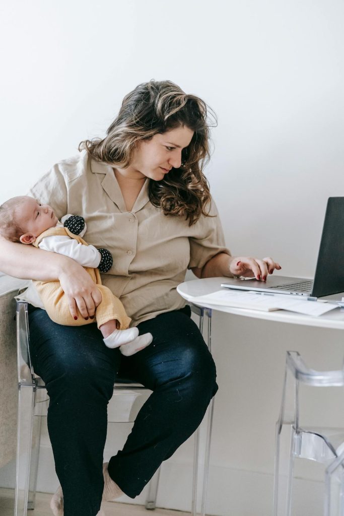 mum holding baby while working on laptop